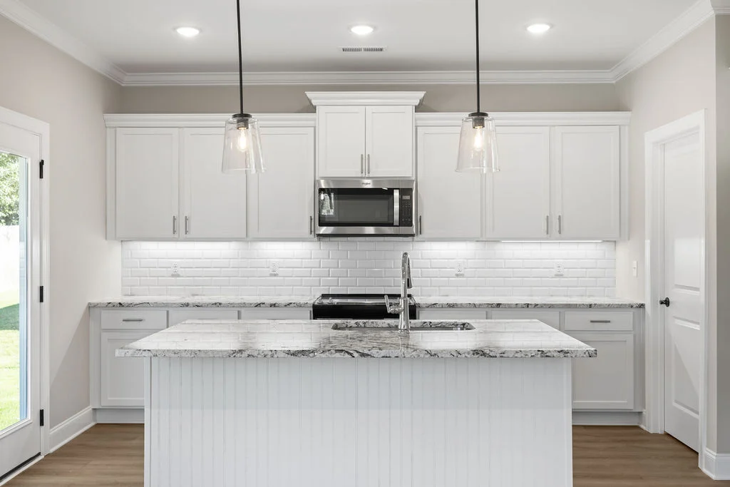 Modern kitchen with white cabinetry, marble countertops, pendant lights, and stainless appliances by Pratt Home Builders in Chattanooga TN.