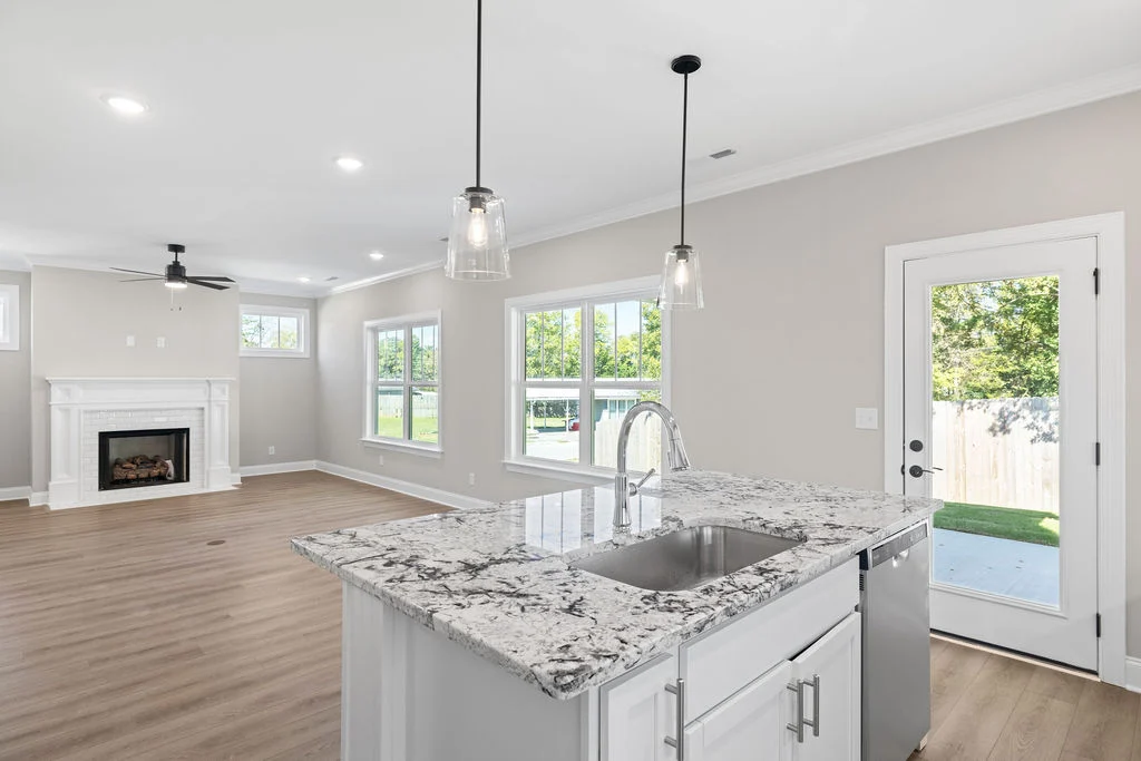Open-concept living area by Pratt Home Builders in Chattanooga TN, featuring a marble island, pendant lights, and a fireplace with outdoor access.