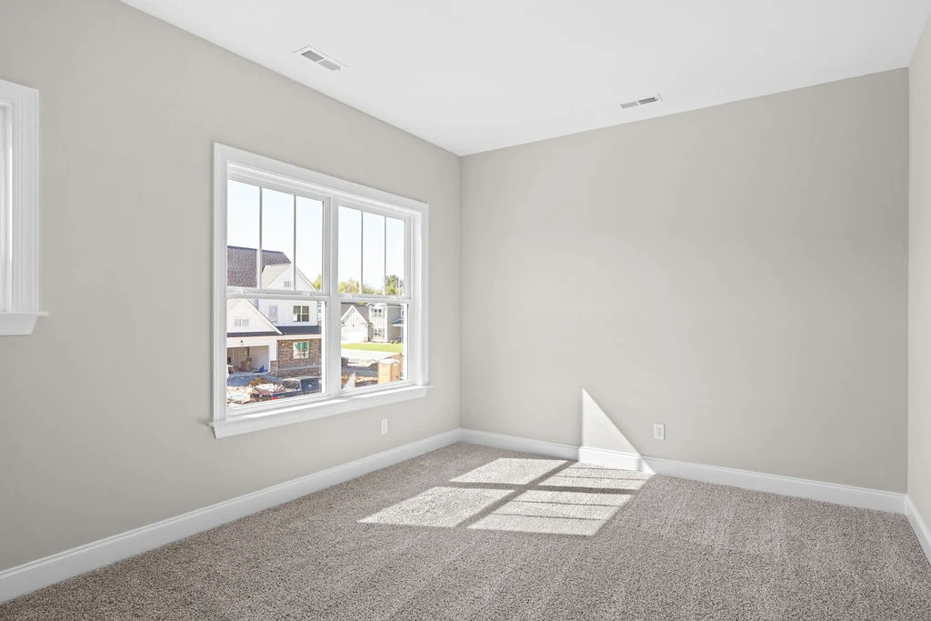 Bright, empty room with beige walls, carpet, and large window. View of suburban homes. Built by Pratt Home Builders in Chattanooga TN.