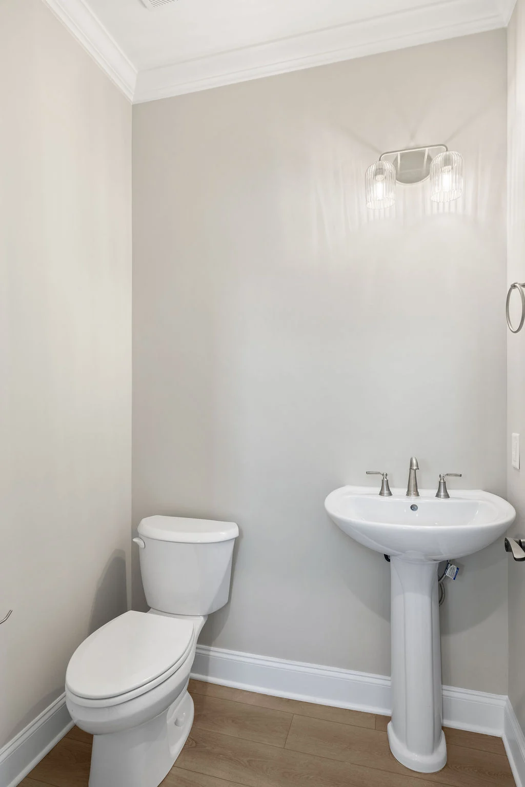 Modern bathroom with pedestal sink, toilet, and wall light fixture. Neutral colors, designed by Pratt Home Builders in Chattanooga TN.