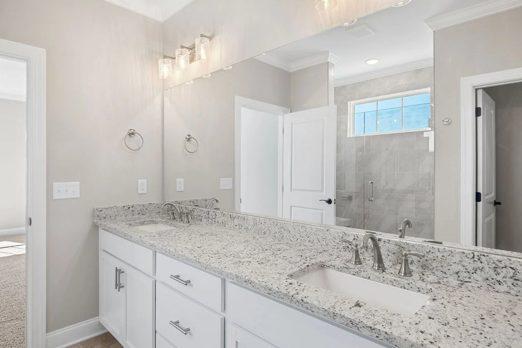 Elegant bathroom by Pratt Home Builders in Chattanooga TN featuring a granite double vanity, large mirror, and tiled shower.