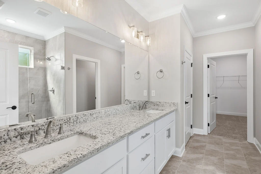 Modern bathroom with dual sinks, granite countertops, and glass shower. Walk-in closet in background. Built by Pratt Home Builders in Chattanooga TN.