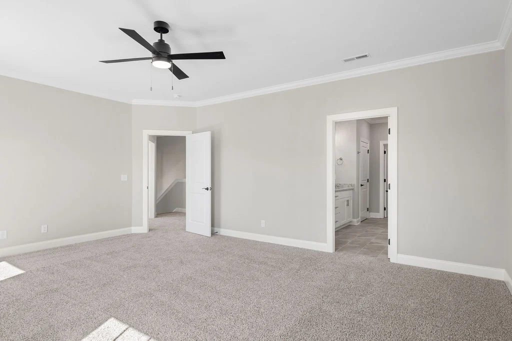 Spacious neutral-toned room with carpet, ceiling fan, doors to hallway and bathroom. Built by Pratt Home Builders in Chattanooga, TN.