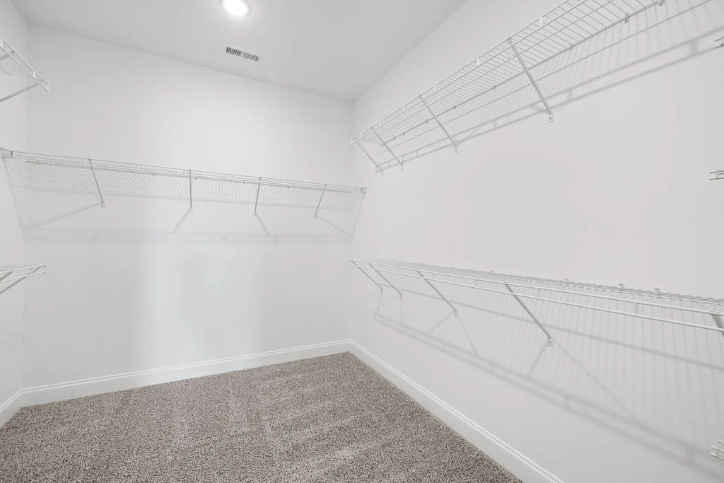 Spacious walk-in closet with white wire shelving, beige carpet, and bright lighting, designed by Pratt Home Builders in Chattanooga TN.