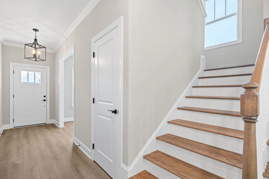 Bright hallway with wooden stairs, white doors, modern light fixture; by Pratt Home Builders in Chattanooga TN.