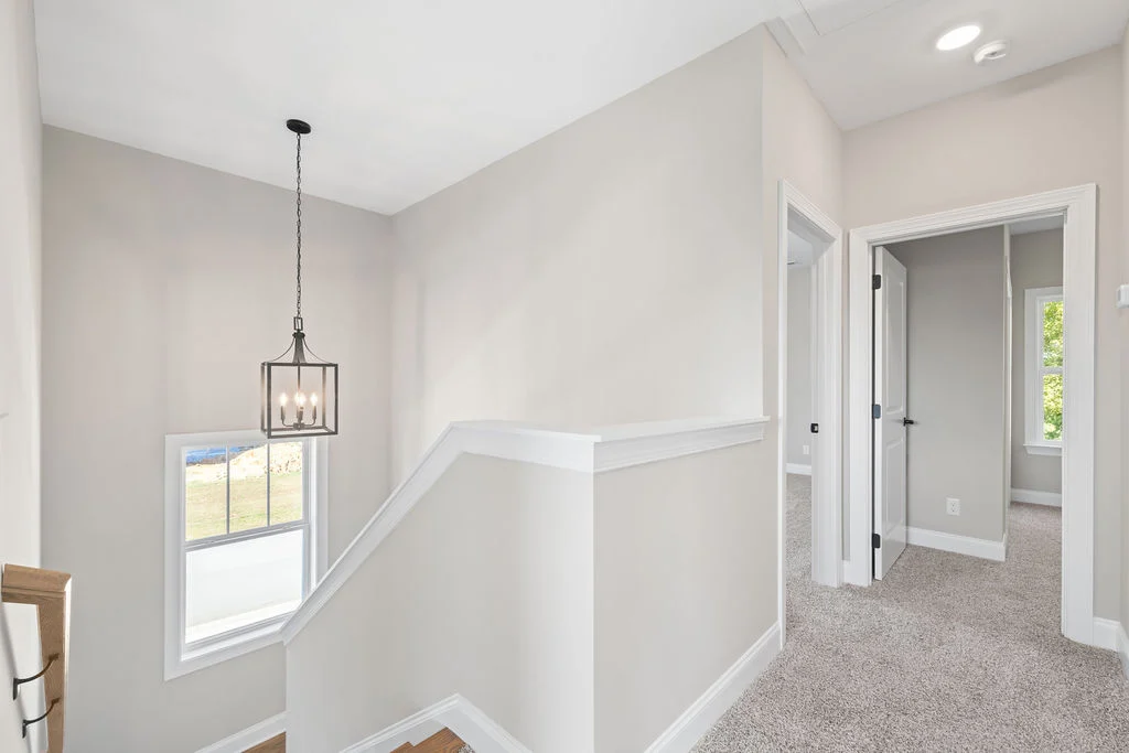 Bright, modern hallway with carpeted floors, neutral walls, and a hanging light fixture by Pratt Home Builders in Chattanooga TN.