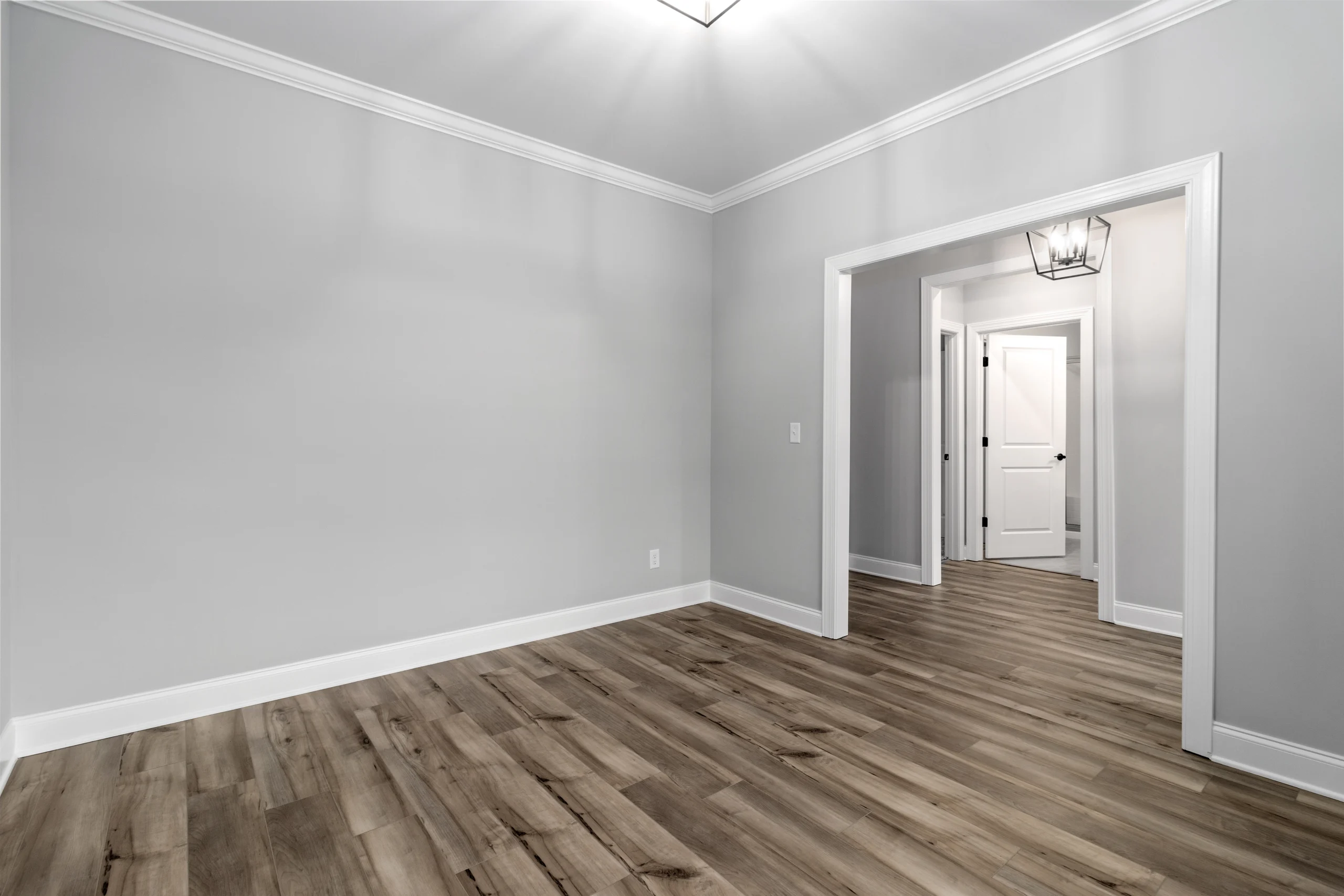 Modern, empty room with wooden floors and gray walls, featuring a doorway leading to a hallway. Design by Pratt Home Builders in Chattanooga TN.