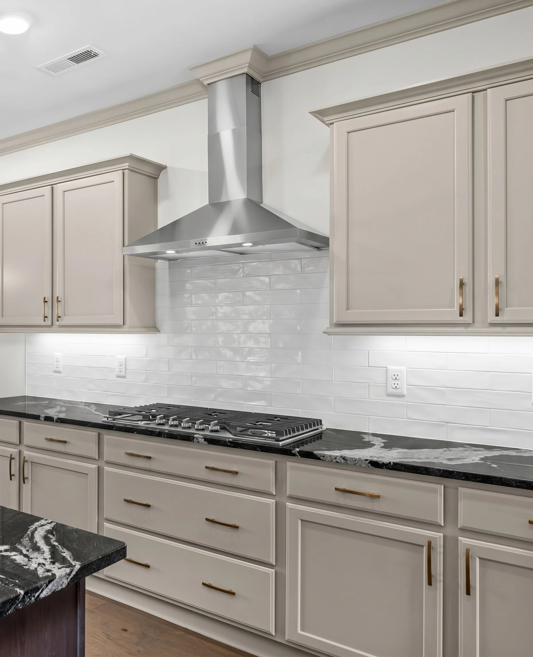 Modern kitchen by Pratt Home Builders in Chattanooga TN, featuring beige cabinets, black marble countertops, and sleek stainless steel vent hood.