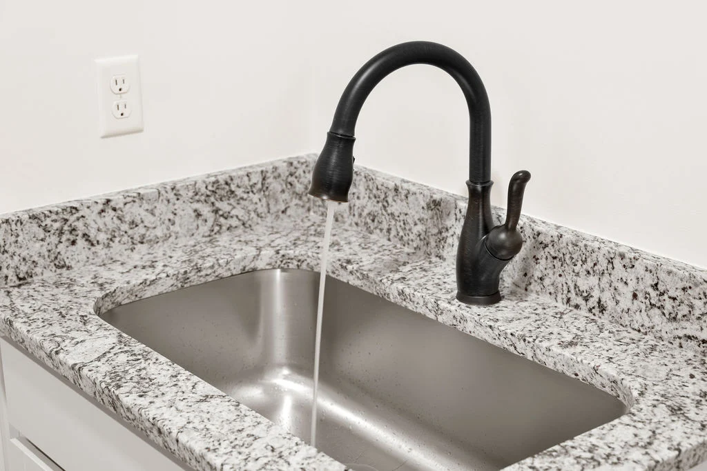 Granite countertop with an elegant black faucet over a metal sink; design by Pratt Home Builders in Chattanooga TN.