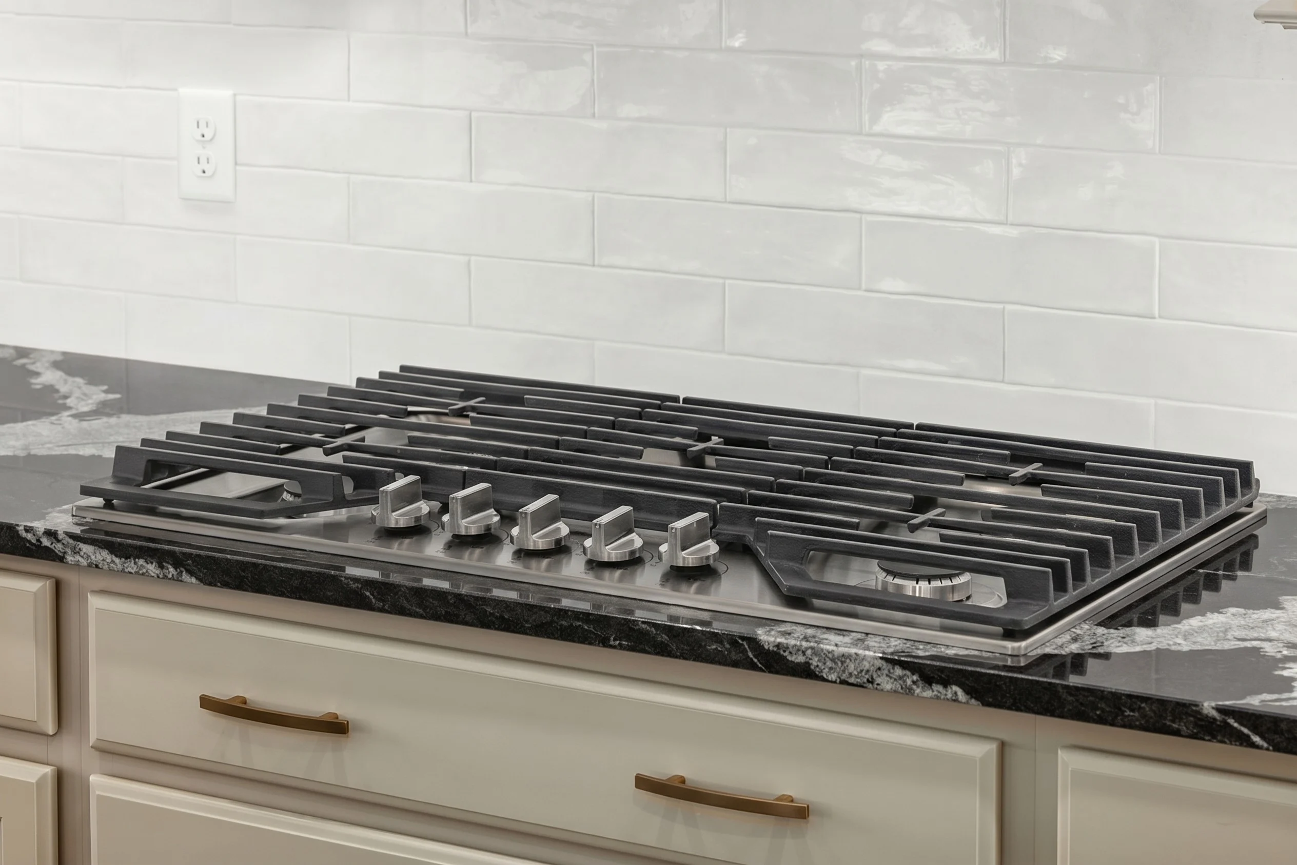 Stainless steel gas cooktop with five burners on black and white marble counter, white tile backsplash. Designed by Pratt Home Builders in Chattanooga