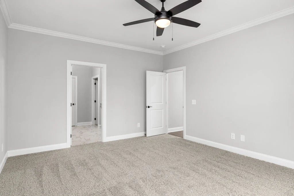 Empty bedroom with gray walls, beige carpet, ceiling fan, and open doors by Pratt Home Builders in Chattanooga TN.