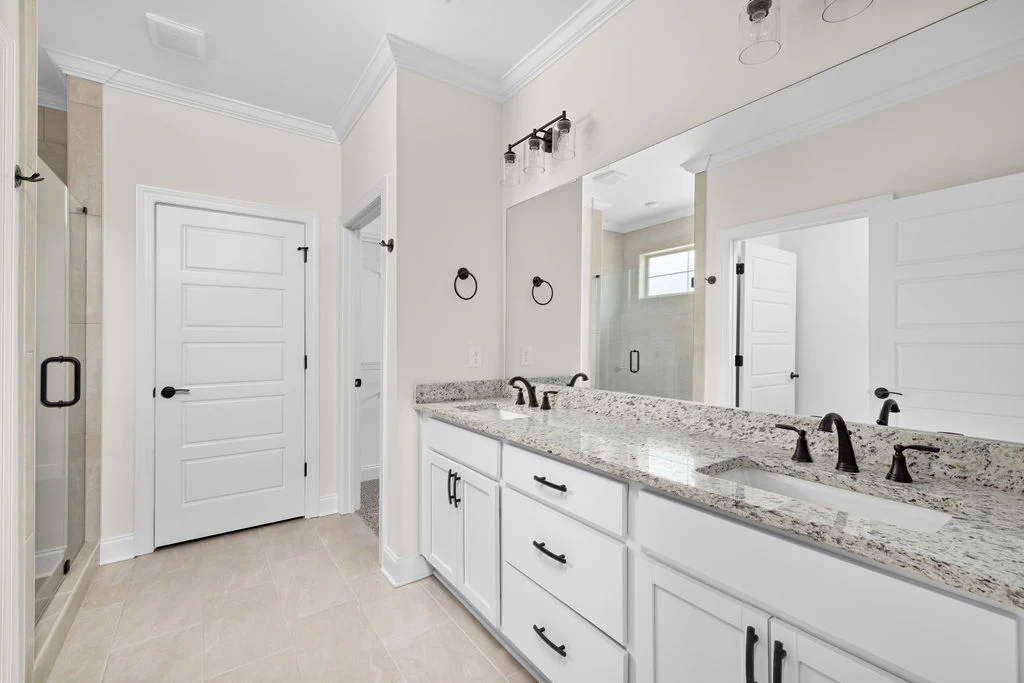 Modern bathroom with dual granite sinks, black fixtures, glass shower, and white cabinetry, designed by Pratt Home Builders in Chattanooga TN.