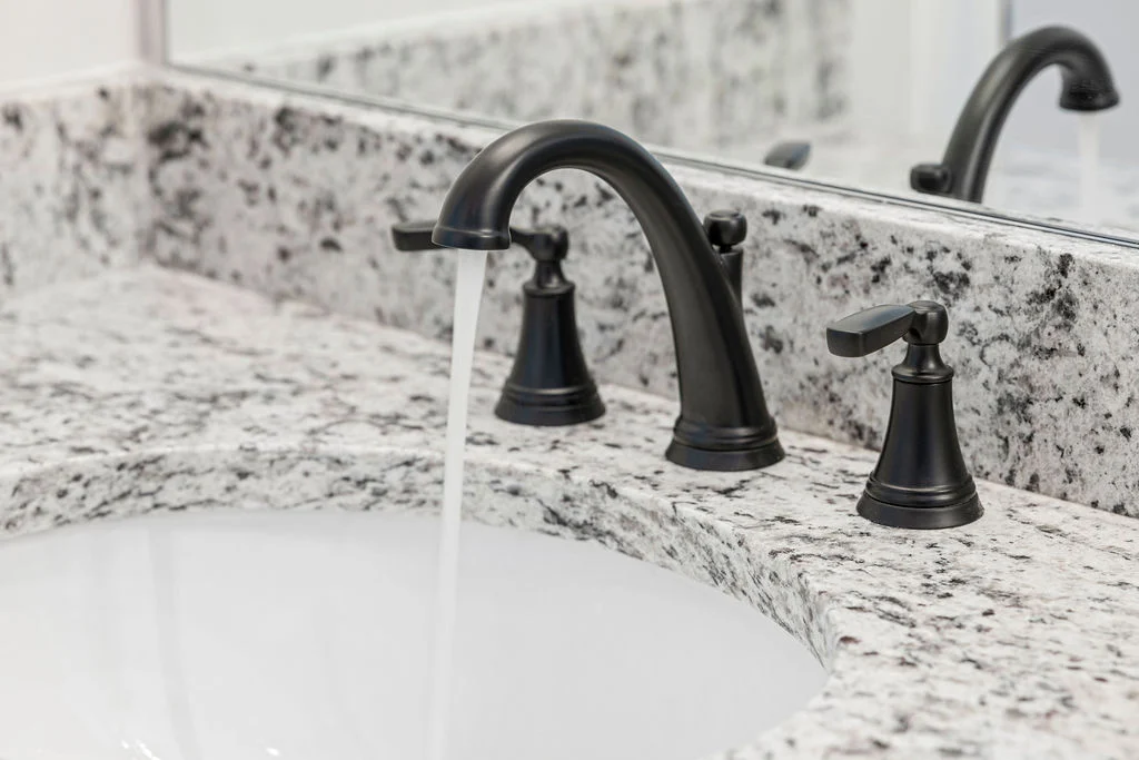 Black faucet with running water on a white granite countertop. Modern bathroom design by Pratt Home Builders in Chattanooga TN.