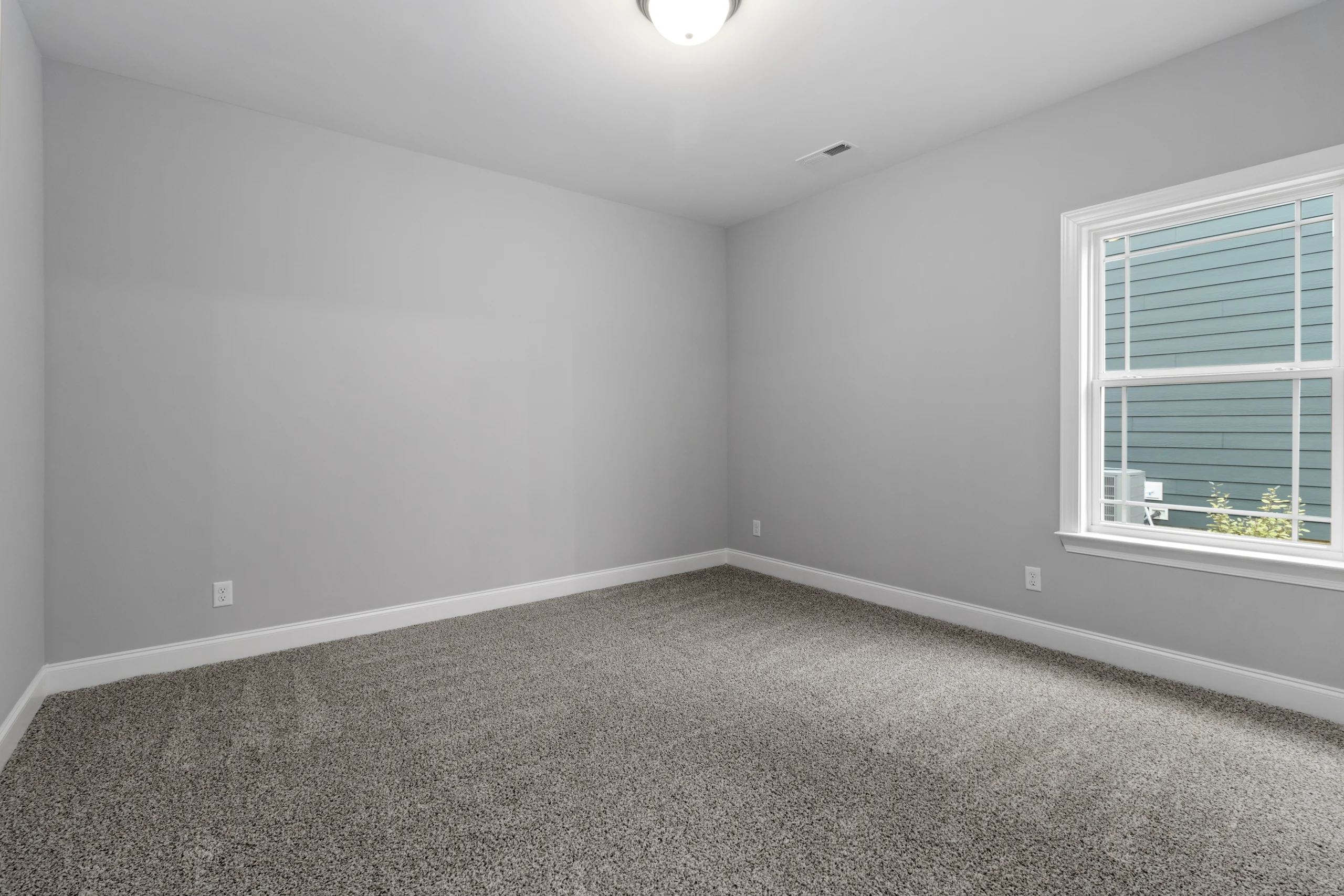Empty gray room with carpeted floor, window view, and ceiling light, designed by Pratt Home Builders in Chattanooga TN.