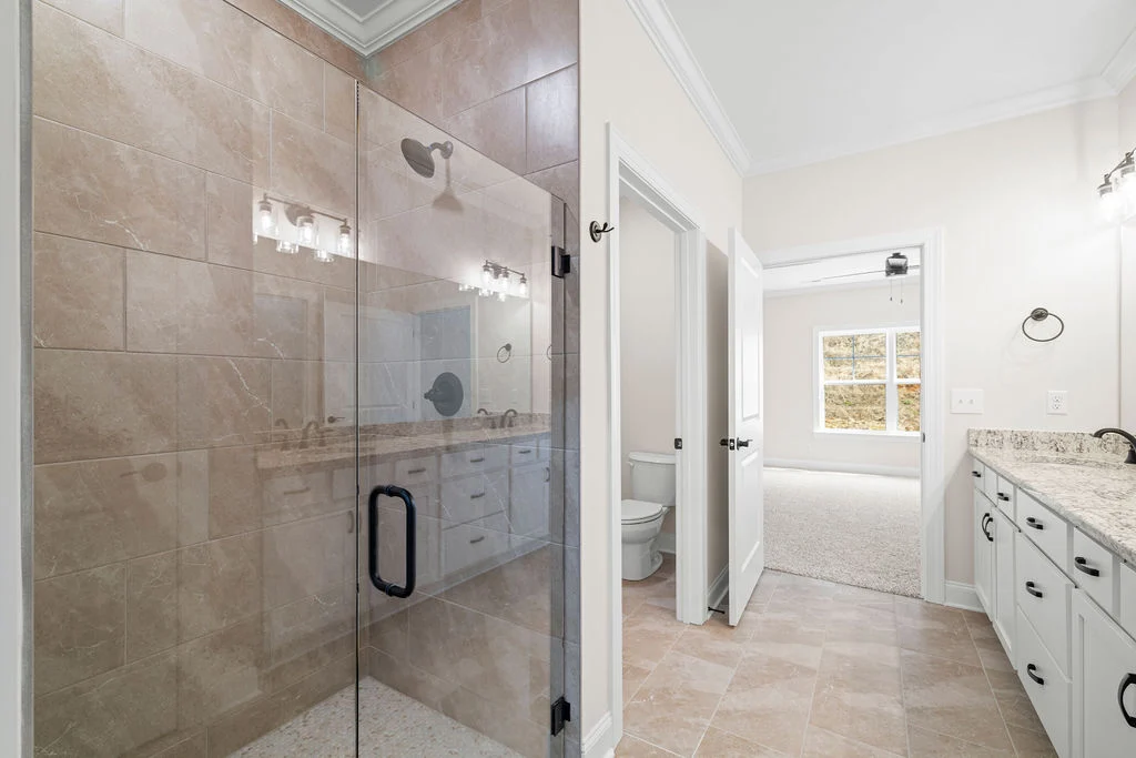 Modern bathroom by Pratt Home Builders in Chattanooga TN, featuring a glass-enclosed shower, dual sinks with granite countertop, and bright lighting.