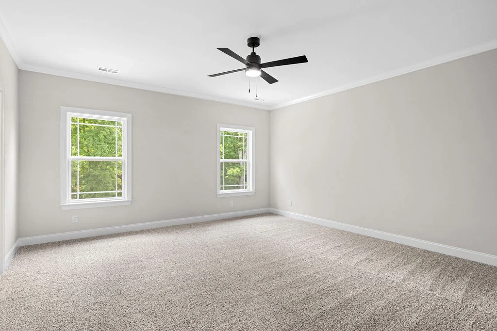 Spacious, carpeted room with neutral walls, ceiling fan, and two windows showcasing greenery. Built by Pratt Home Builders in Chattanooga TN.