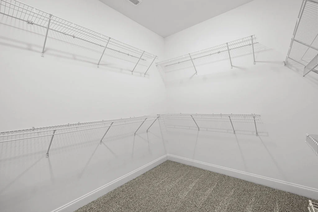 Spacious walk-in closet with white wire shelving by Pratt Home Builders in Chattanooga TN, featuring clean lines and a plush carpeted floor.