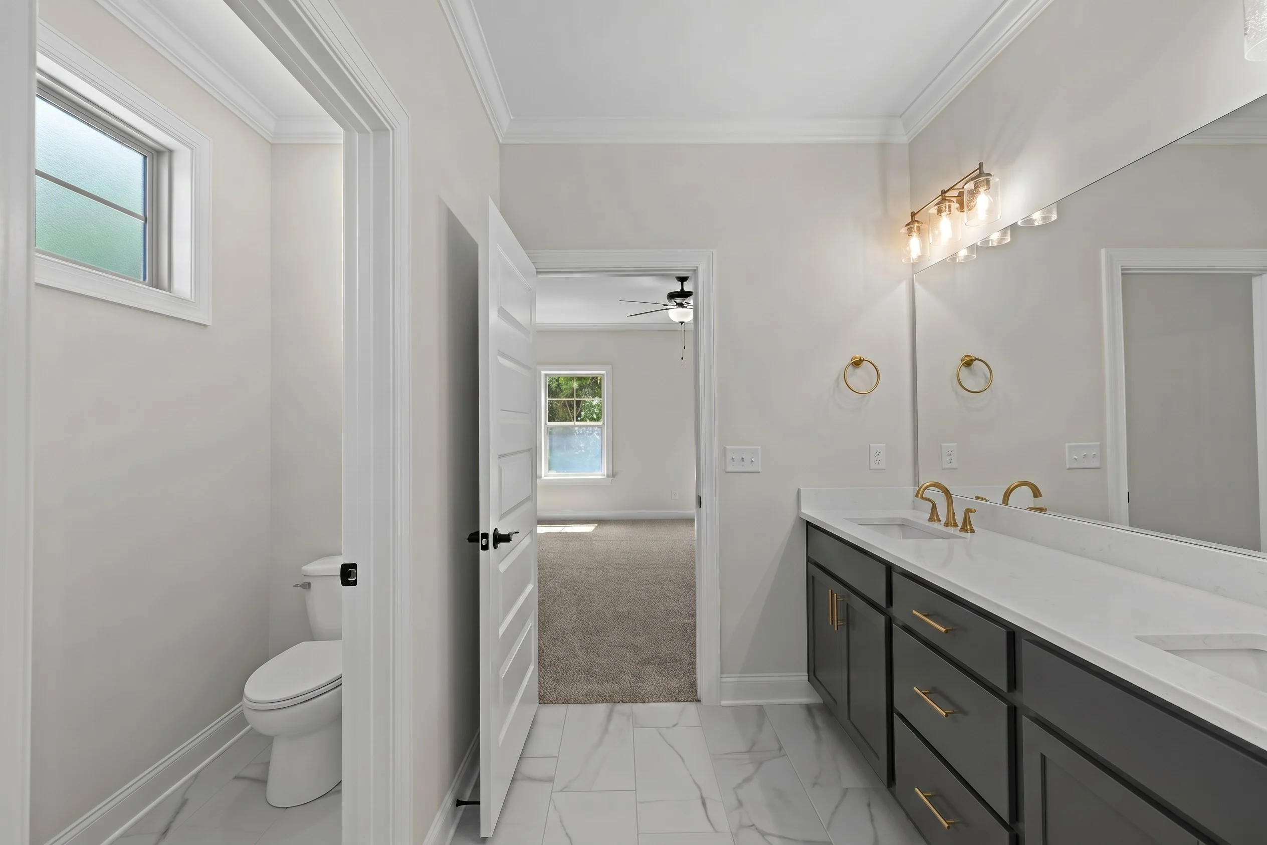 Modern bathroom by Pratt Home Builders in Chattanooga TN, featuring dual sinks, marble flooring, and a view into a carpeted bedroom.