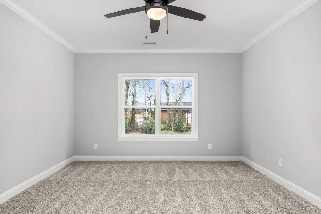 Empty room with gray walls, carpet, ceiling fan, and large window overlooking trees. Built by Pratt Home Builders in Chattanooga TN.