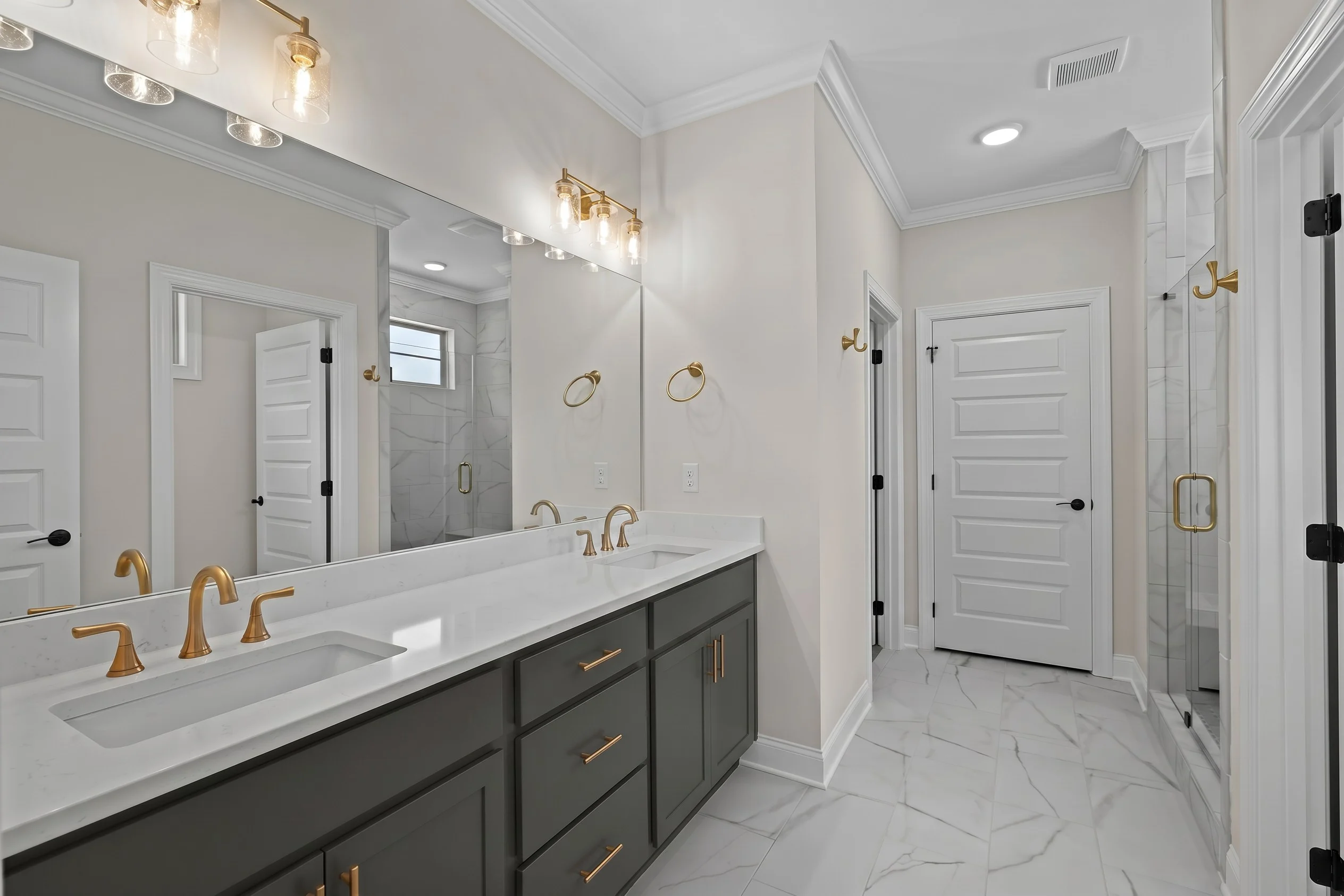 Elegant bathroom by Pratt Home Builders in Chattanooga TN, featuring dual sinks, brass fixtures, marble tiles, and glass shower doors.