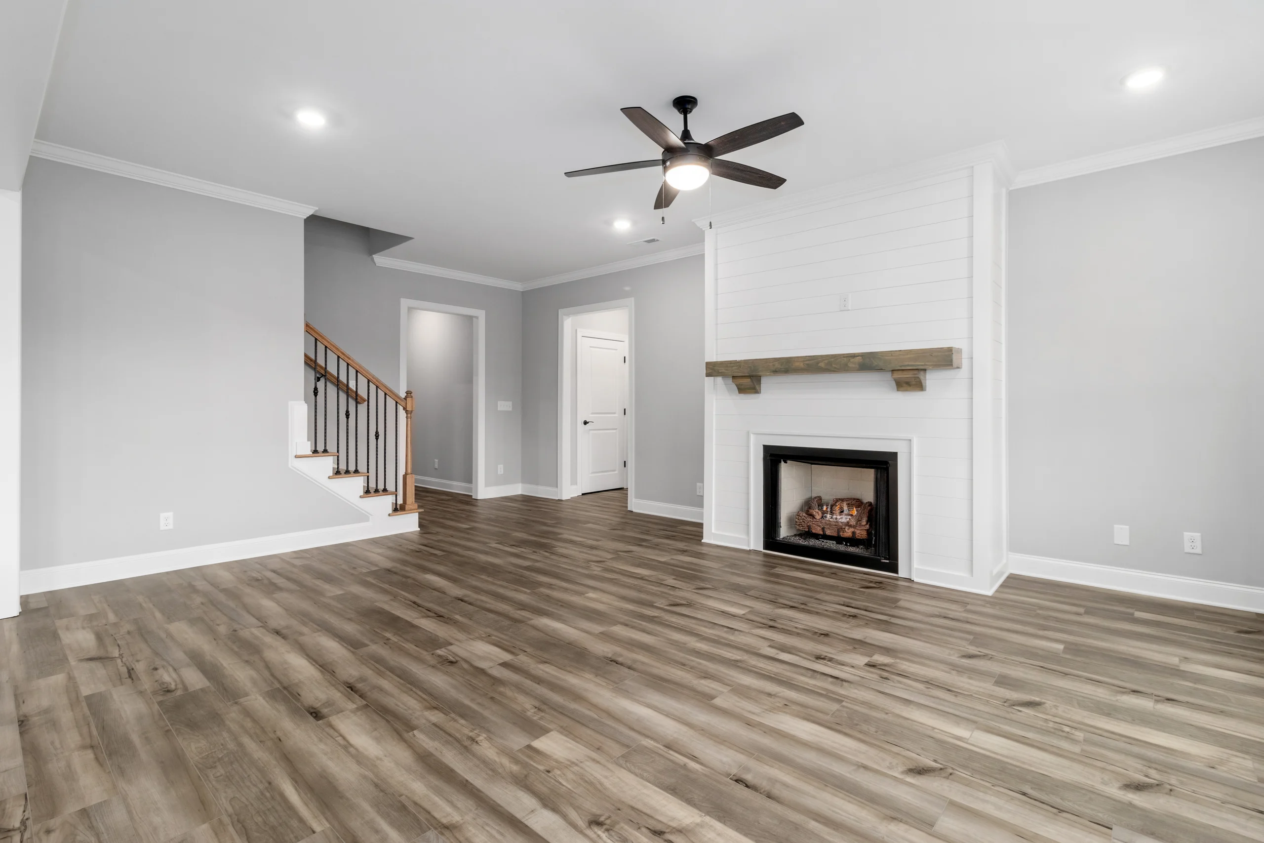Modern living room by Pratt Home Builders in Chattanooga TN, featuring a fireplace, wood flooring, ceiling fan, and staircase with iron railing.