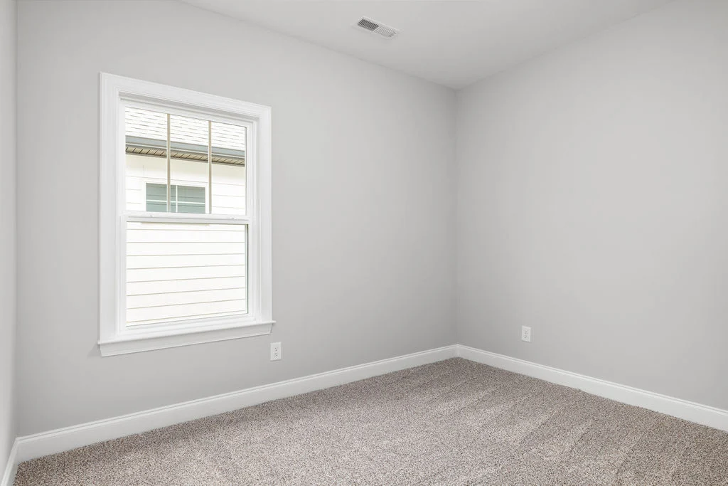 Empty room with light gray walls and carpet, featuring a single window. Built by Pratt Home Builders in Chattanooga TN.