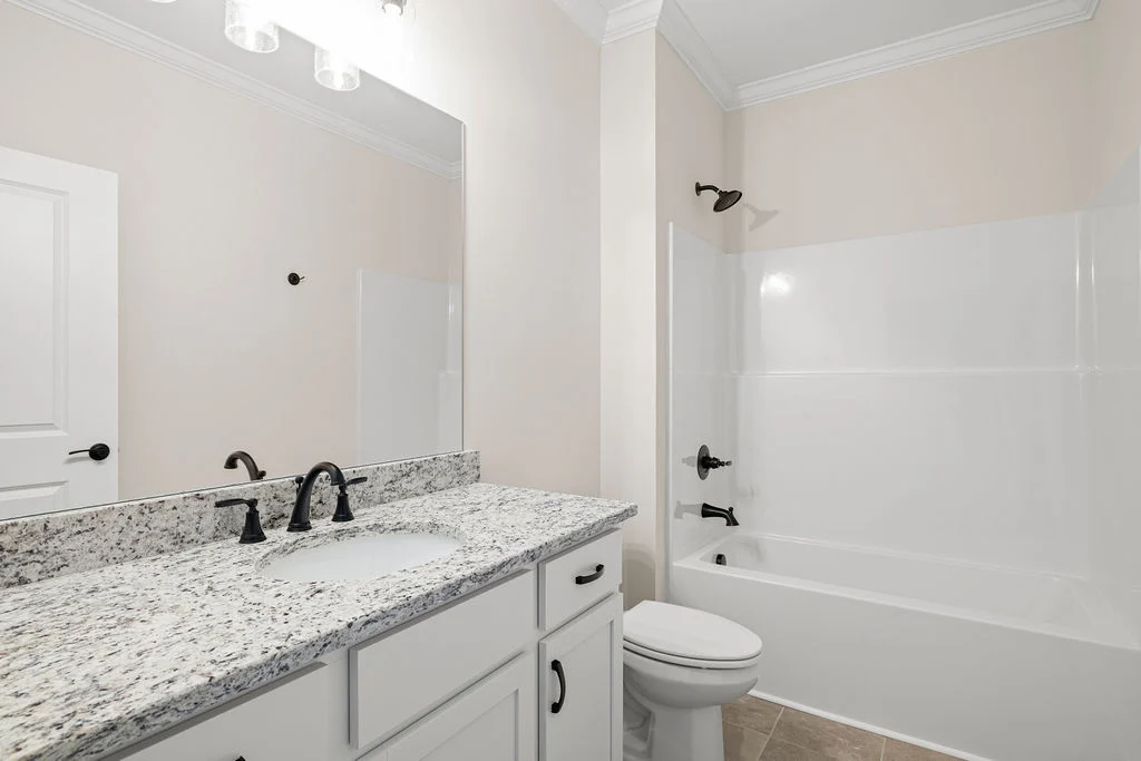 Modern bathroom with granite countertop, black fixtures, white cabinets, and a bathtub by Pratt Home Builders in Chattanooga TN.