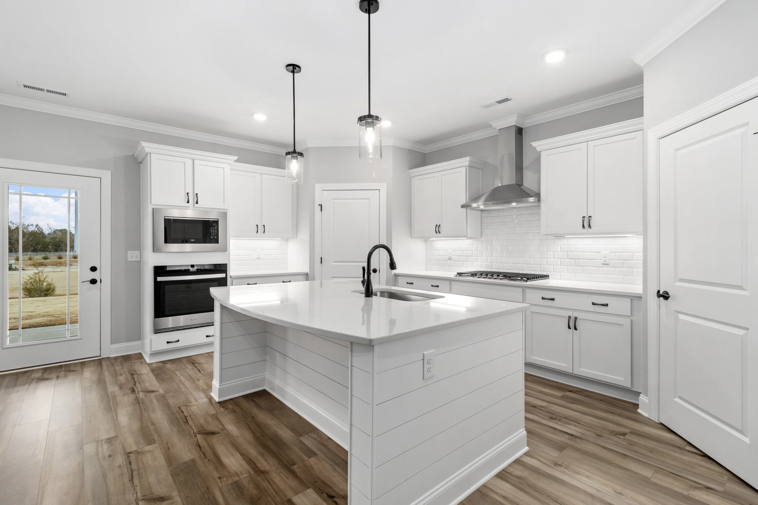 Modern kitchen by Pratt Home Builders in Chattanooga TN, featuring white cabinets, island, sleek appliances, and wood flooring.