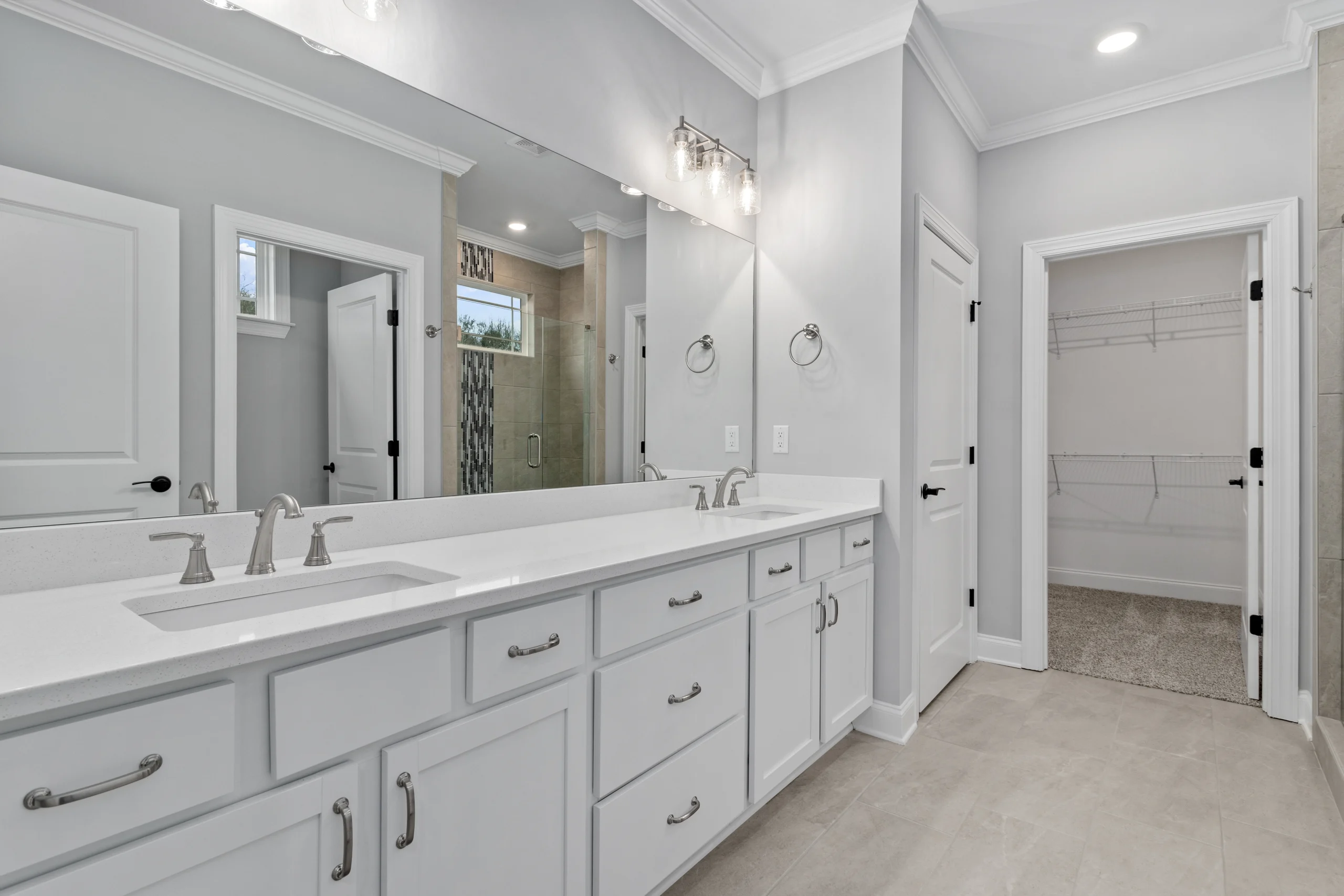 Modern bathroom with dual sinks, white cabinetry, large mirror, and walk-in closet, by Pratt Home Builders in Chattanooga TN.