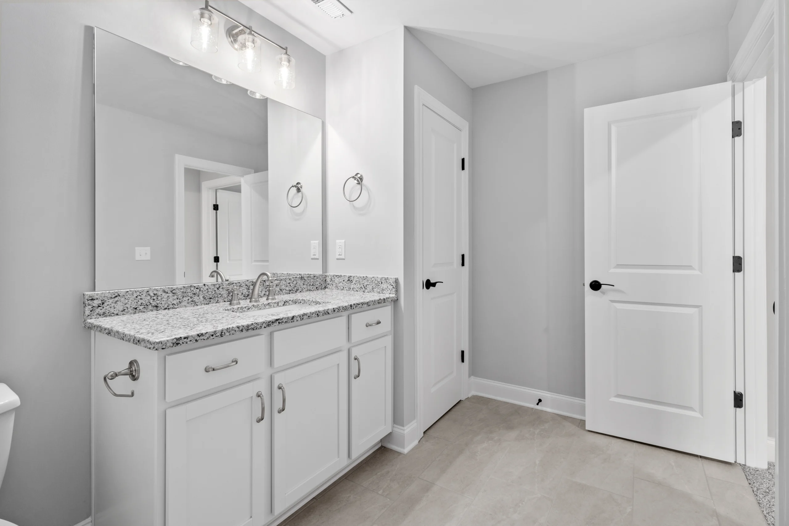 Modern bathroom by Pratt Home Builders in Chattanooga TN, featuring granite countertop, dual sinks, large mirror, and white cabinetry.