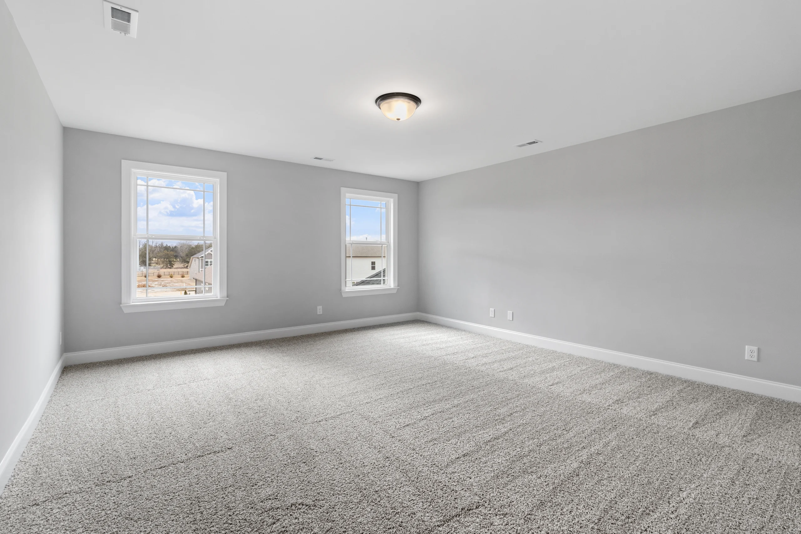 Spacious, light-filled room with gray carpet and walls, featuring two windows. Built by Pratt Home Builders in Chattanooga TN.