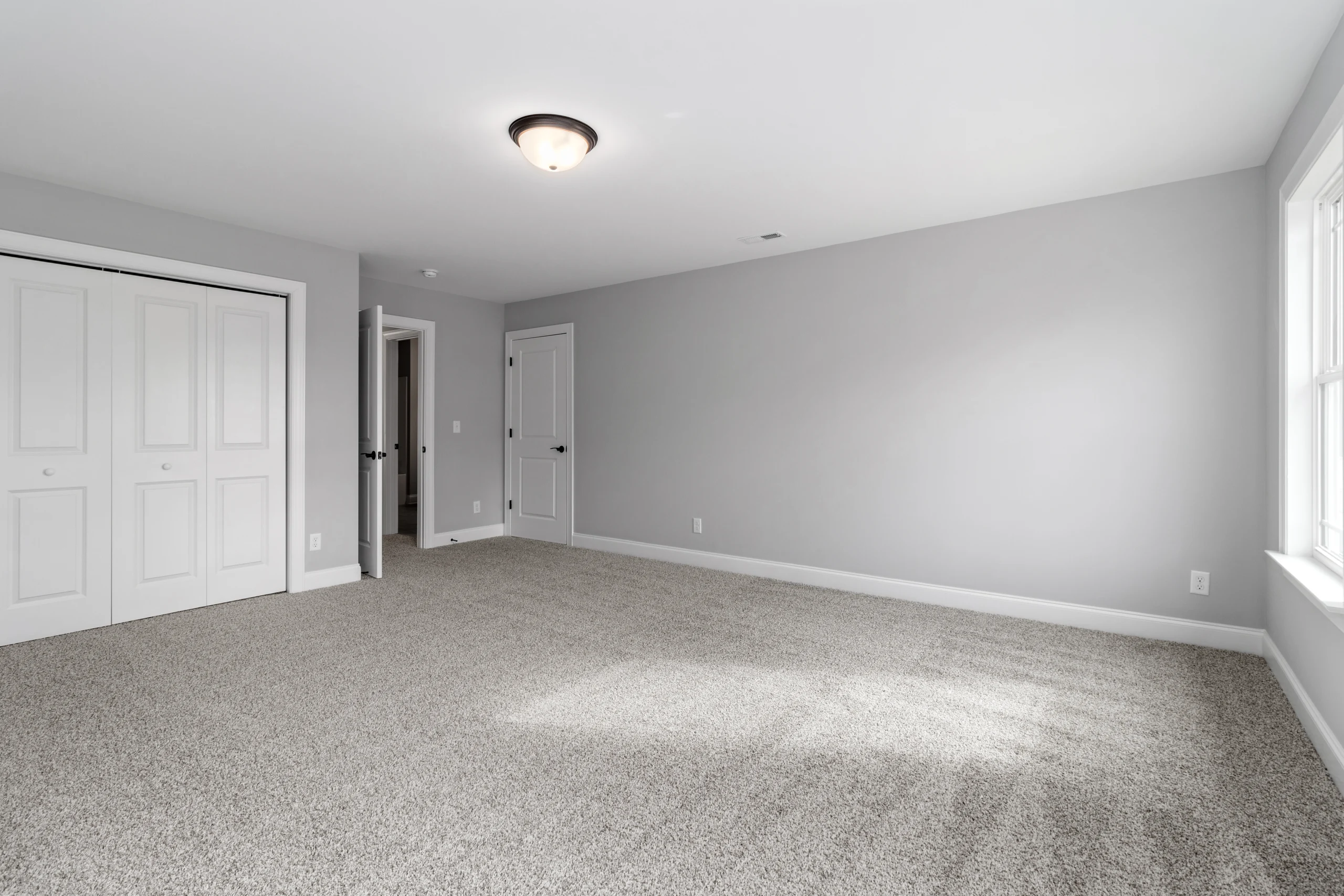 Spacious, carpeted room with gray walls, white doors, and ample natural light from a window, designed by Pratt Home Builders in Chattanooga TN.