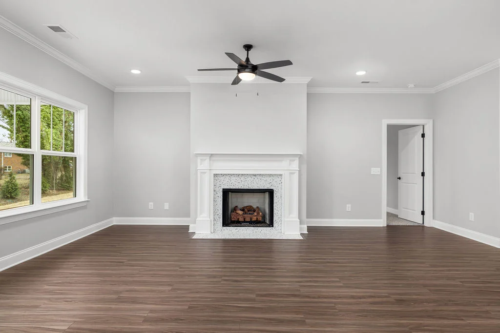 Spacious modern living room by Pratt Home Builders in Chattanooga TN, featuring a cozy fireplace, gray walls, and a ceiling fan.
