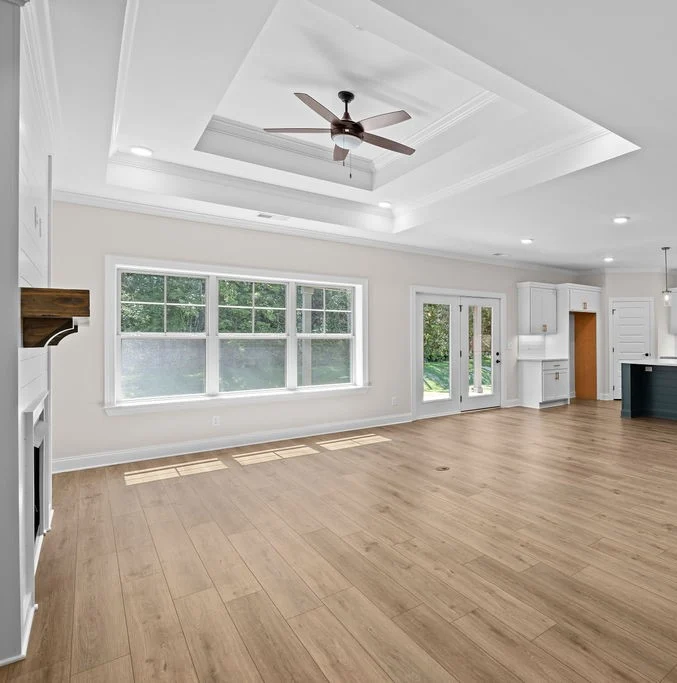 Spacious living area with wood floors, tray ceiling, large windows, and French doors. Modern design by Pratt Home Builders in Chattanooga TN.