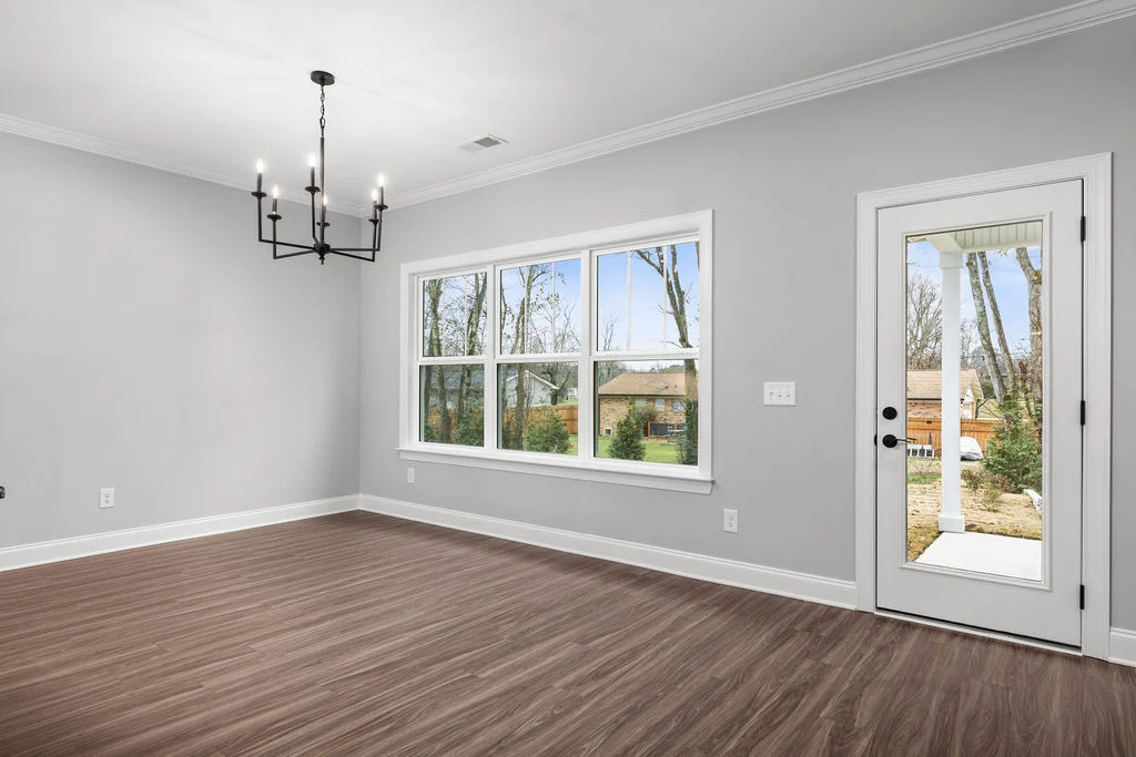Bright, minimalist room by Pratt Home Builders in Chattanooga TN, featuring wood floors, a large window, and a glass door overlooking a backyard.