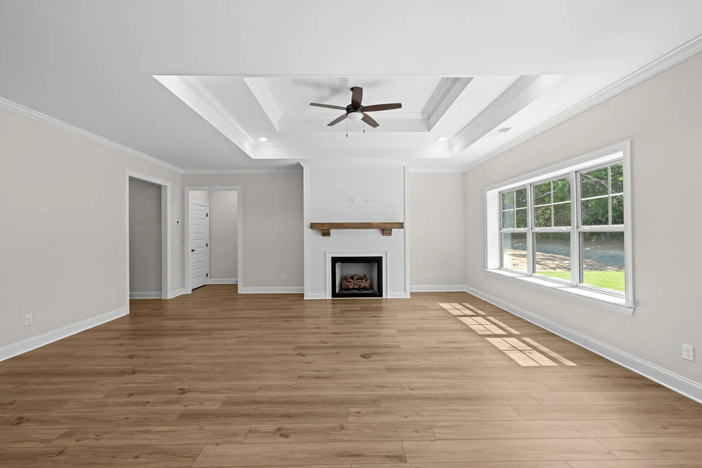 Spacious living room with tray ceiling, fireplace, ceiling fan, and large windows designed by Pratt Home Builders in Chattanooga TN.