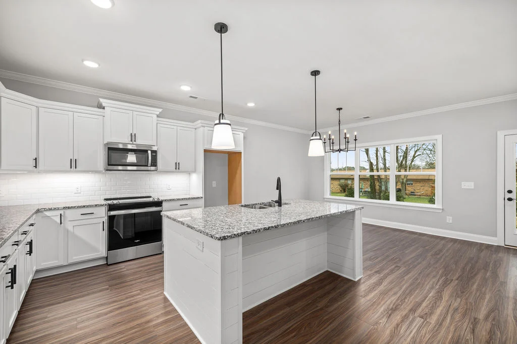 Modern kitchen and dining area with white cabinets, granite countertops, and wood flooring by Pratt Home Builders in Chattanooga TN.