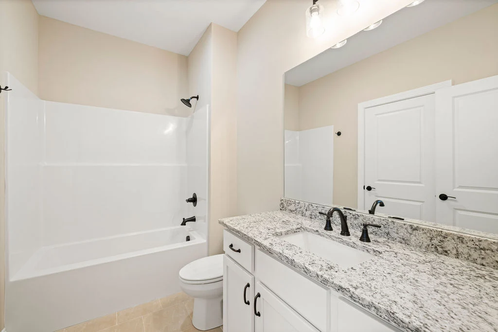 Modern bathroom featuring a granite countertop, dual sinks, and a bathtub with black fixtures by Pratt Home Builders in Chattanooga TN.