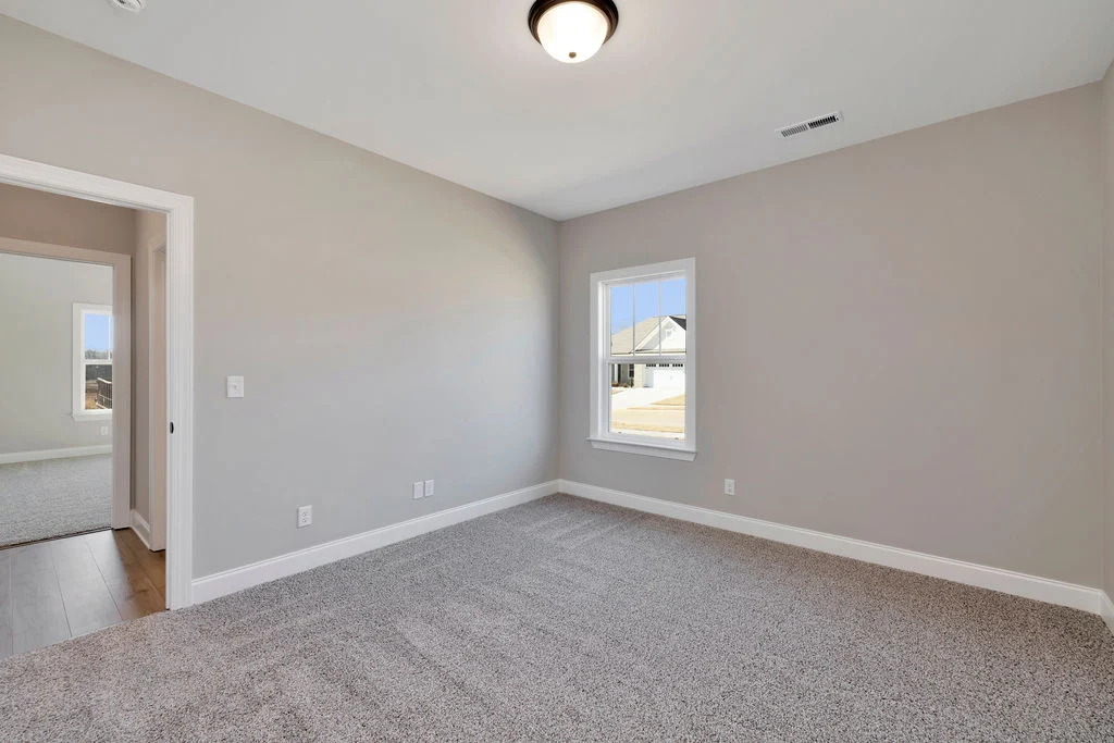 Empty room with gray carpet, beige walls, and a window showing a suburban street. Built by Pratt Home Builders in Chattanooga TN.