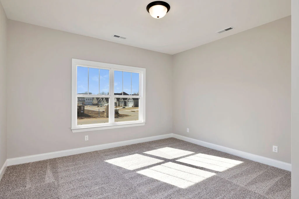 Bright empty room with beige walls, large window, and carpet flooring by Pratt Home Builders in Chattanooga TN.
