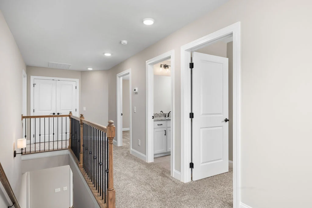 Bright, carpeted upstairs hallway with wooden railings, open doors, and soft lighting by Pratt Home Builders in Chattanooga TN.