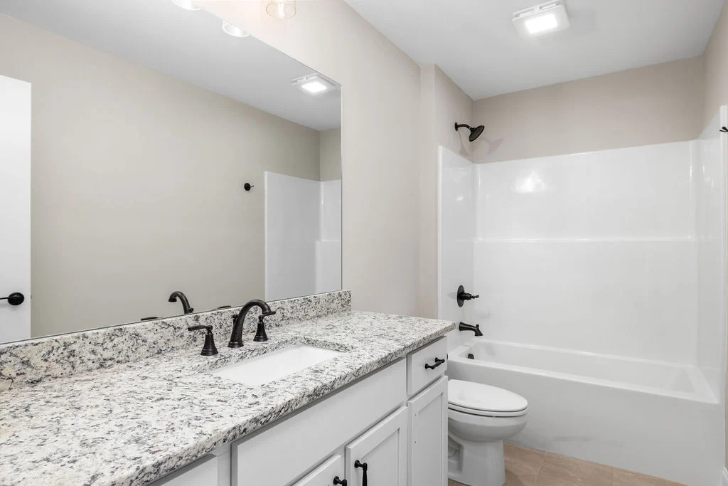 Modern bathroom with granite countertop, white cabinets, and a tub-shower combo. Designed by Pratt Home Builders in Chattanooga TN.