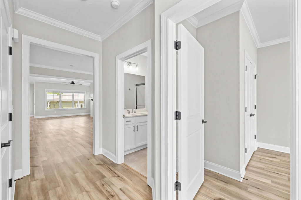 Hallway with light wood floors, leading to rooms with white doors and a bright, open living area. Designed by Pratt Home Builders in Chattanooga TN.