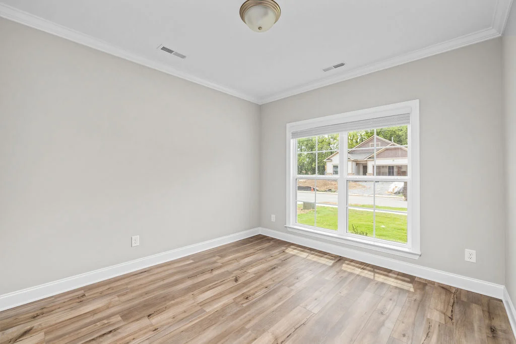 Bright, empty room with wood flooring, neutral walls, large window overlooking a suburban street. Designed by Pratt Home Builders in Chattanooga TN.