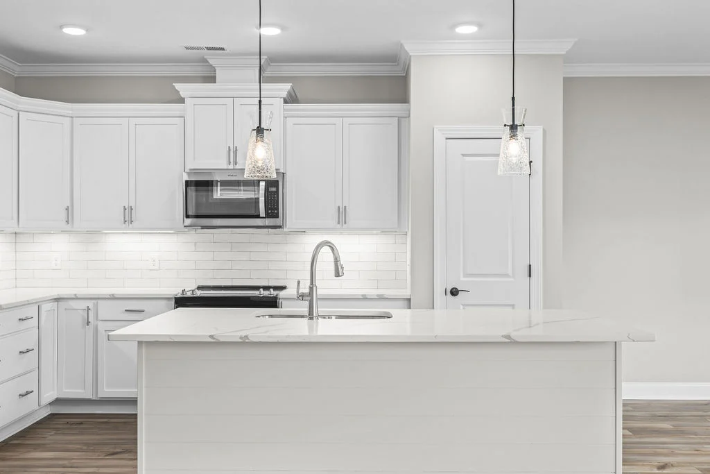 Modern kitchen with white cabinetry, island, pendant lights, and stainless steel appliances. Pratt Home Builders in Chattanooga TN design.