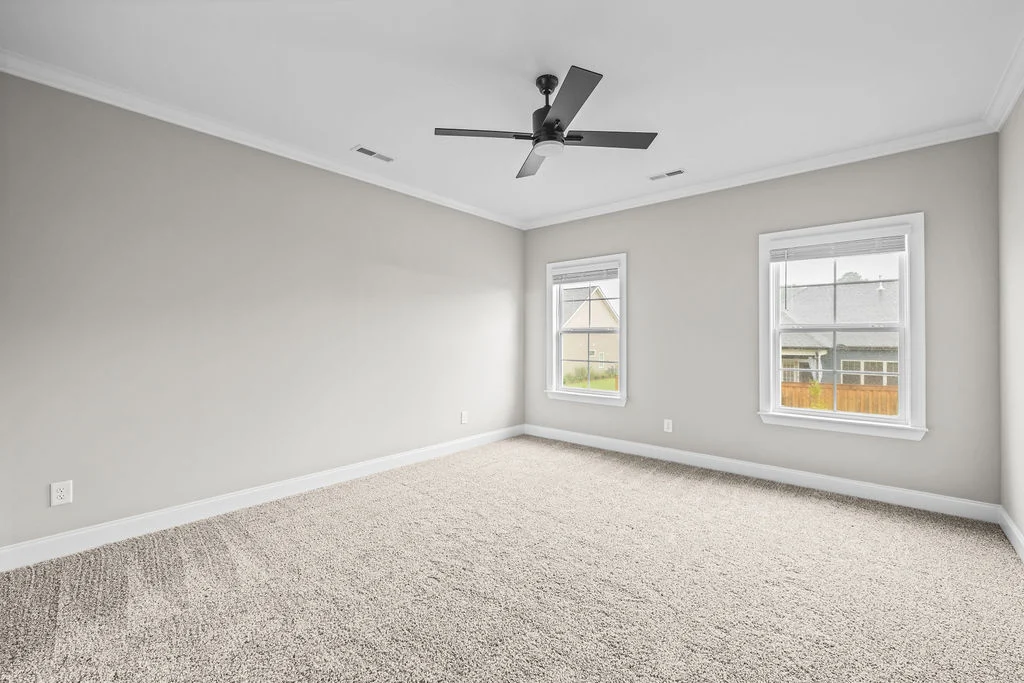 Empty carpeted room with light gray walls, two windows, and ceiling fan. Built by Pratt Home Builders in Chattanooga TN.