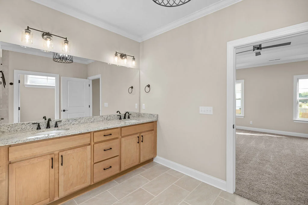 Modern bathroom by Pratt Home Builders in Chattanooga TN, granite double vanity, light wood cabinets, and view into a sunlit carpeted bedroom.