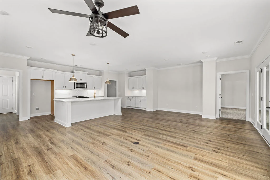 Spacious kitchen by Pratt Home Builders in Chattanooga TN, featuring white cabinetry, pendant lights, and wood flooring in an open-plan layout.