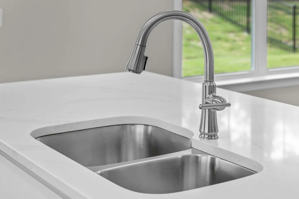 Modern kitchen sink with a sleek stainless steel faucet on a white countertop by Pratt Home Builders in Chattanooga TN, adjacent to a window.
