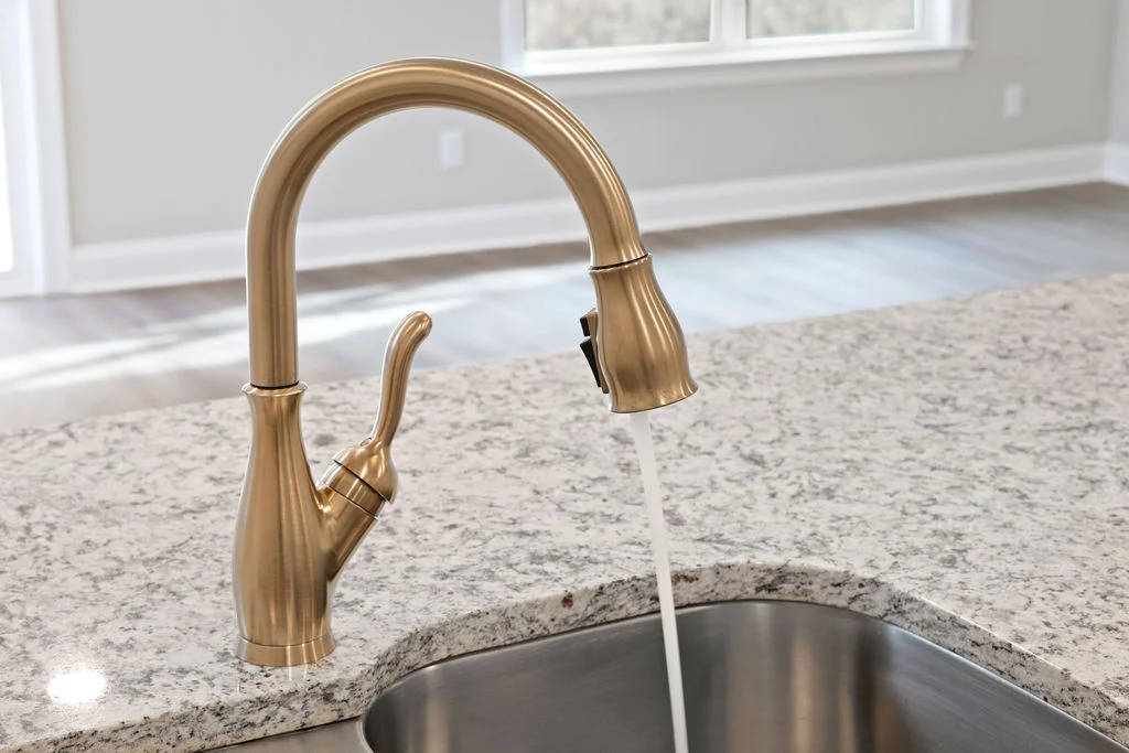 Gold kitchen faucet with running water on marble countertop, designed by Pratt Home Builders in Chattanooga TN.